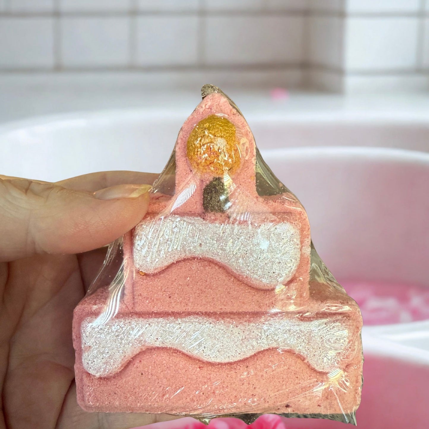 Pink and white layered soap with gold center held by a hand against a blurred background