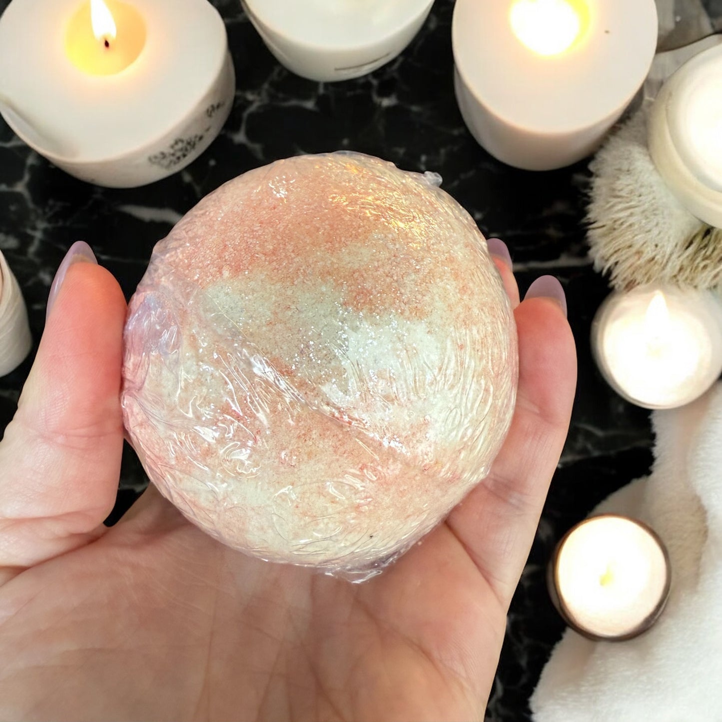 Hand holding a wrapped bath bomb with candles in the background