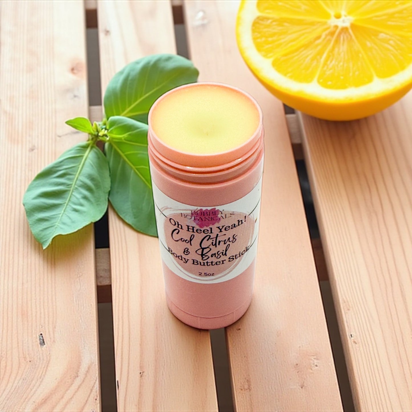 Pink body butter stick with a label on a wooden surface next to a lemon and leaves