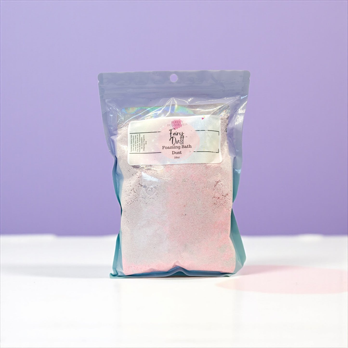 Packaged pink bath salt with a label on a white surface and purple background
