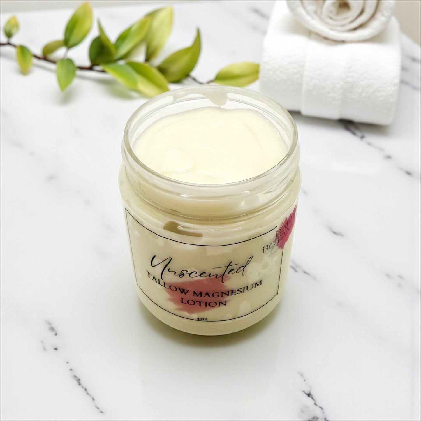 Jar of unscented lotion on a marble surface with a white towel and green leaves.