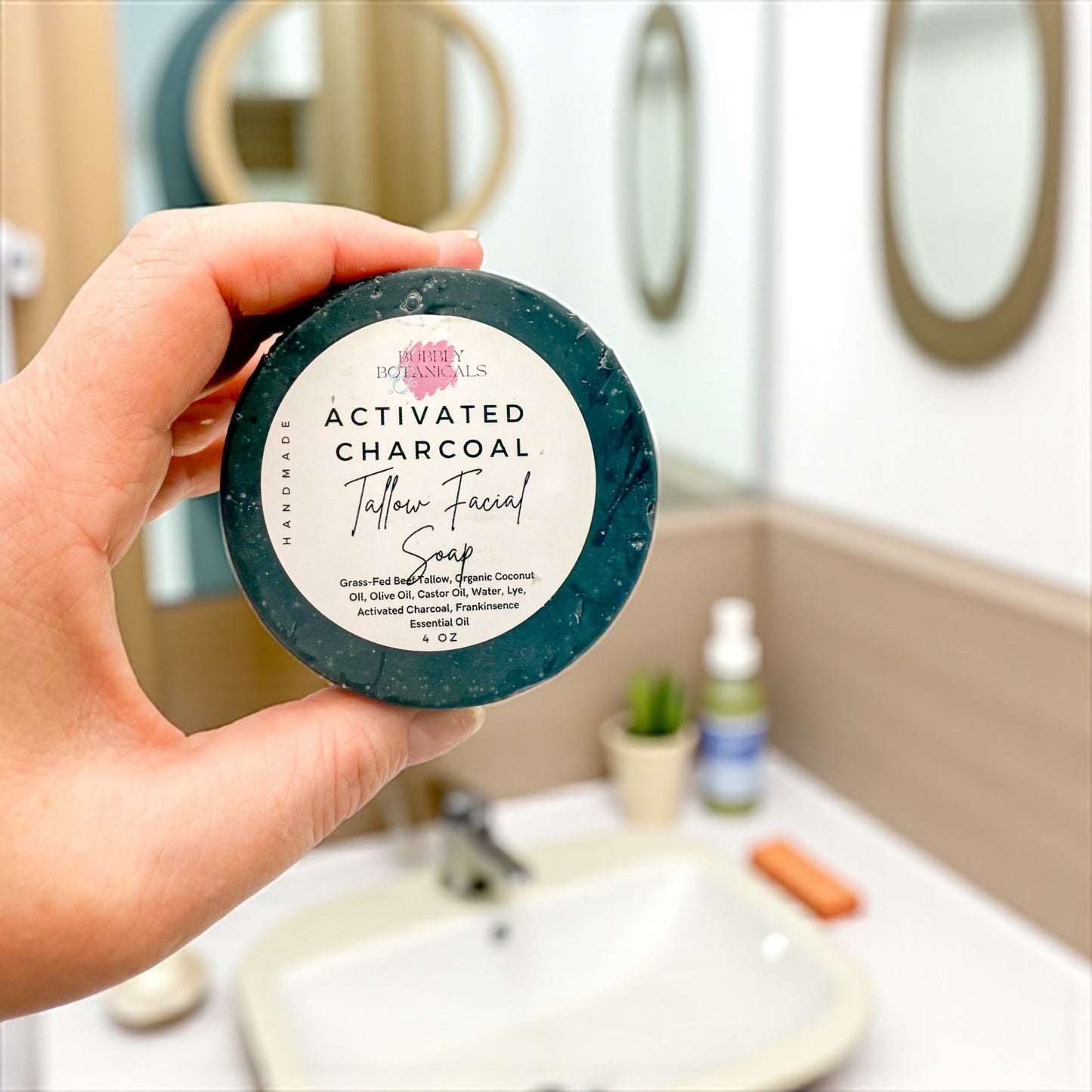 Hand holding a bar of activated charcoal soap with a bathroom background