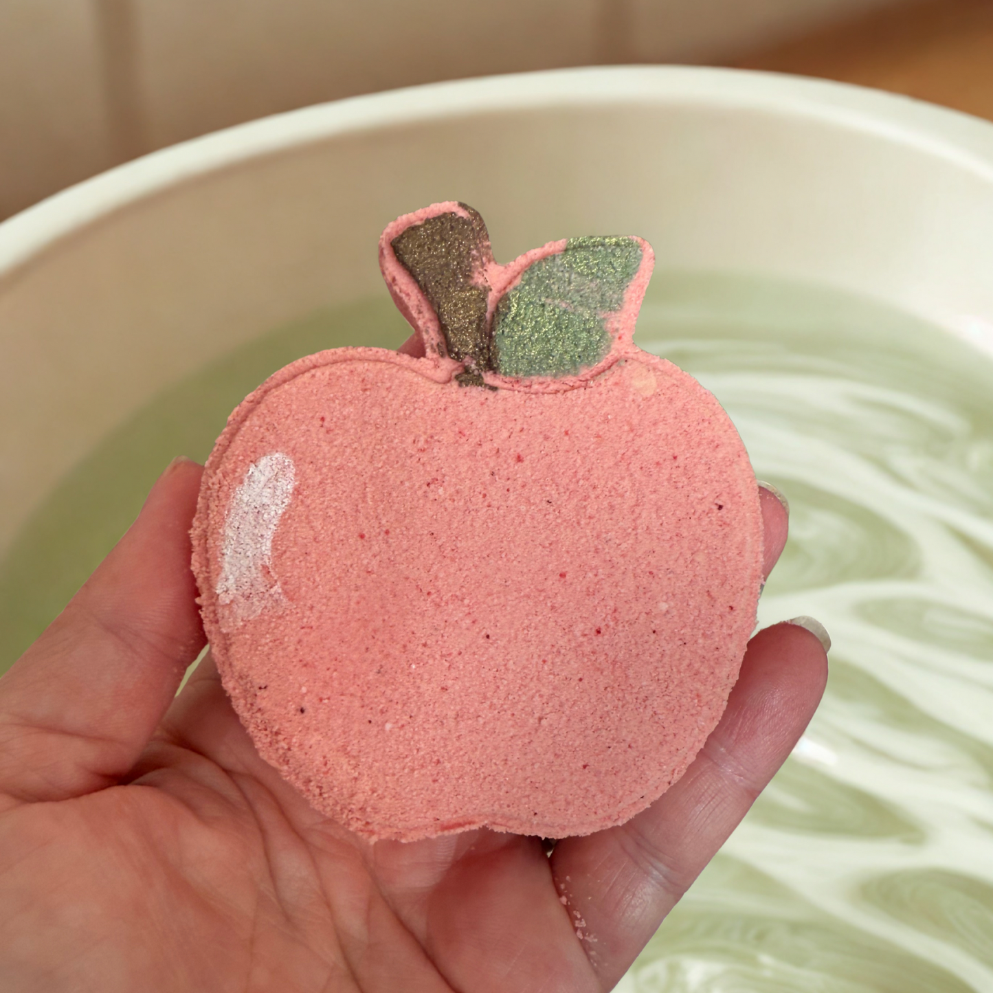 Pink apple-shaped bath bomb held over a bathtub