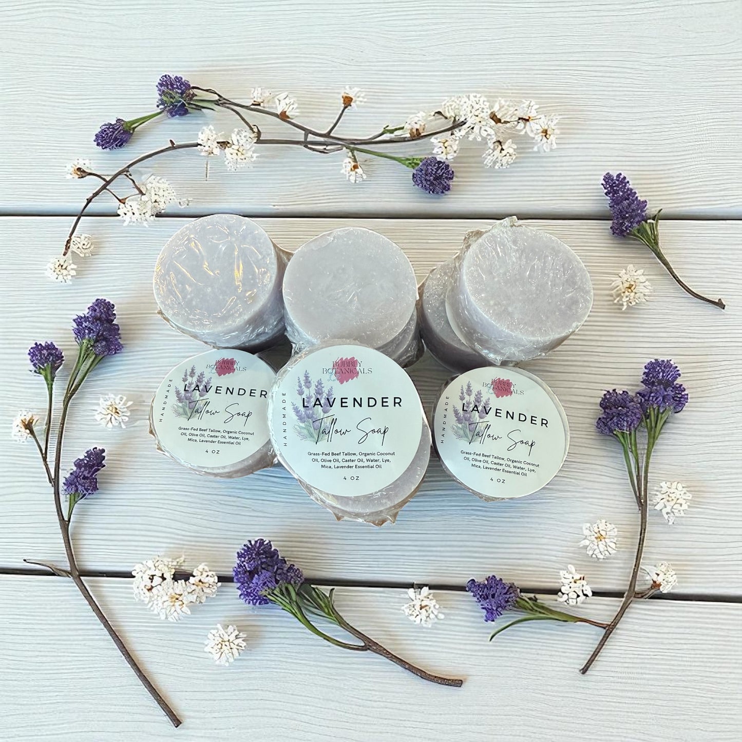 Lavender tallow soaps on a white wood table with lavender buds all around