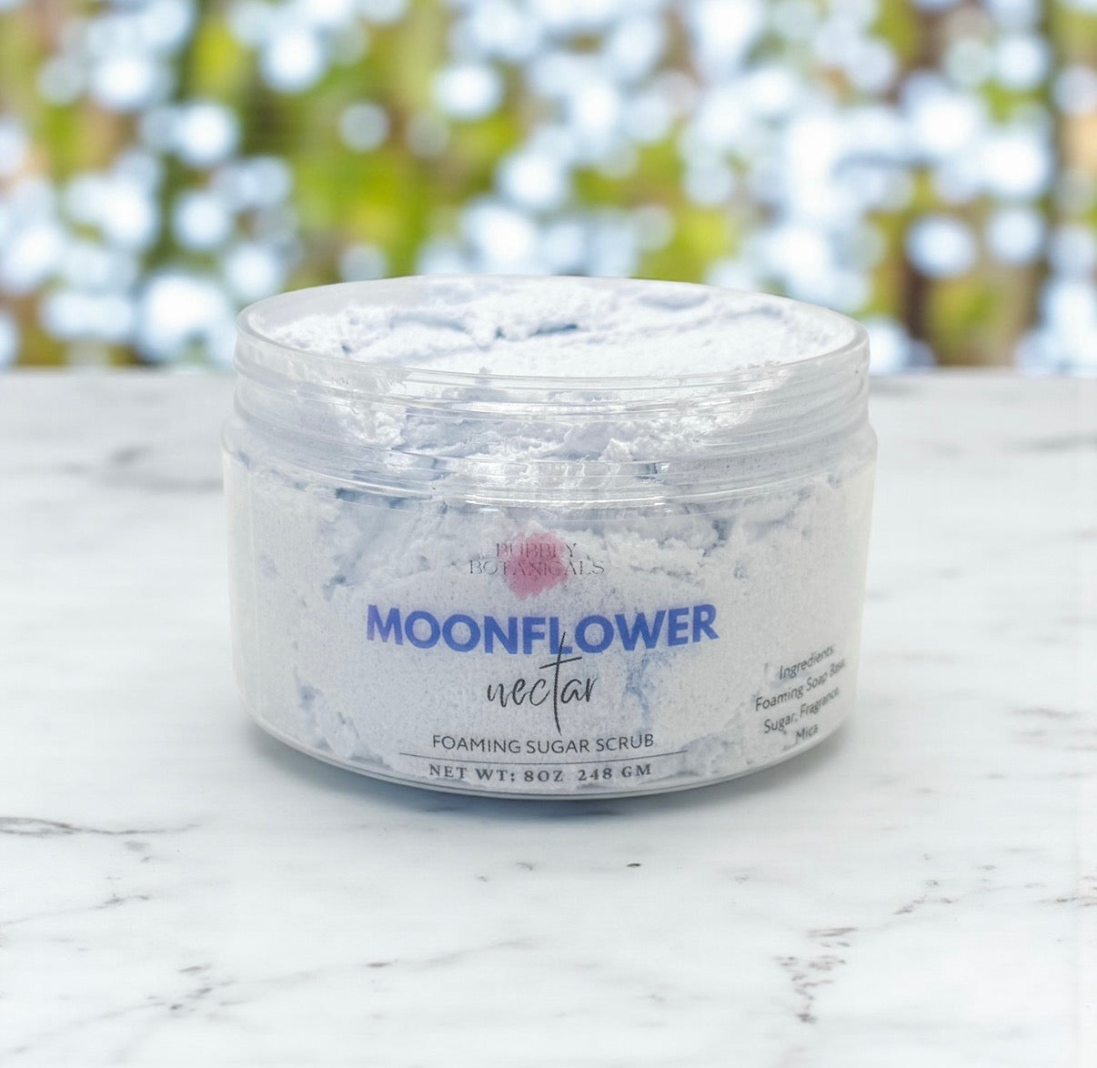 Jar of Moonflower Nectar foaming sugar scrub on a marble surface with blurred greenery in the background