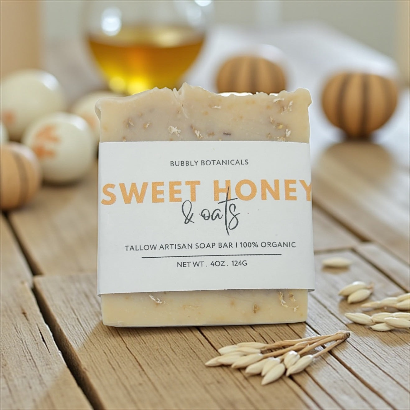 Bar of tallow soap labeled 'Sweet Honey & Oats' from Bubbly Botanicals on a wooden surface with honey and oats.