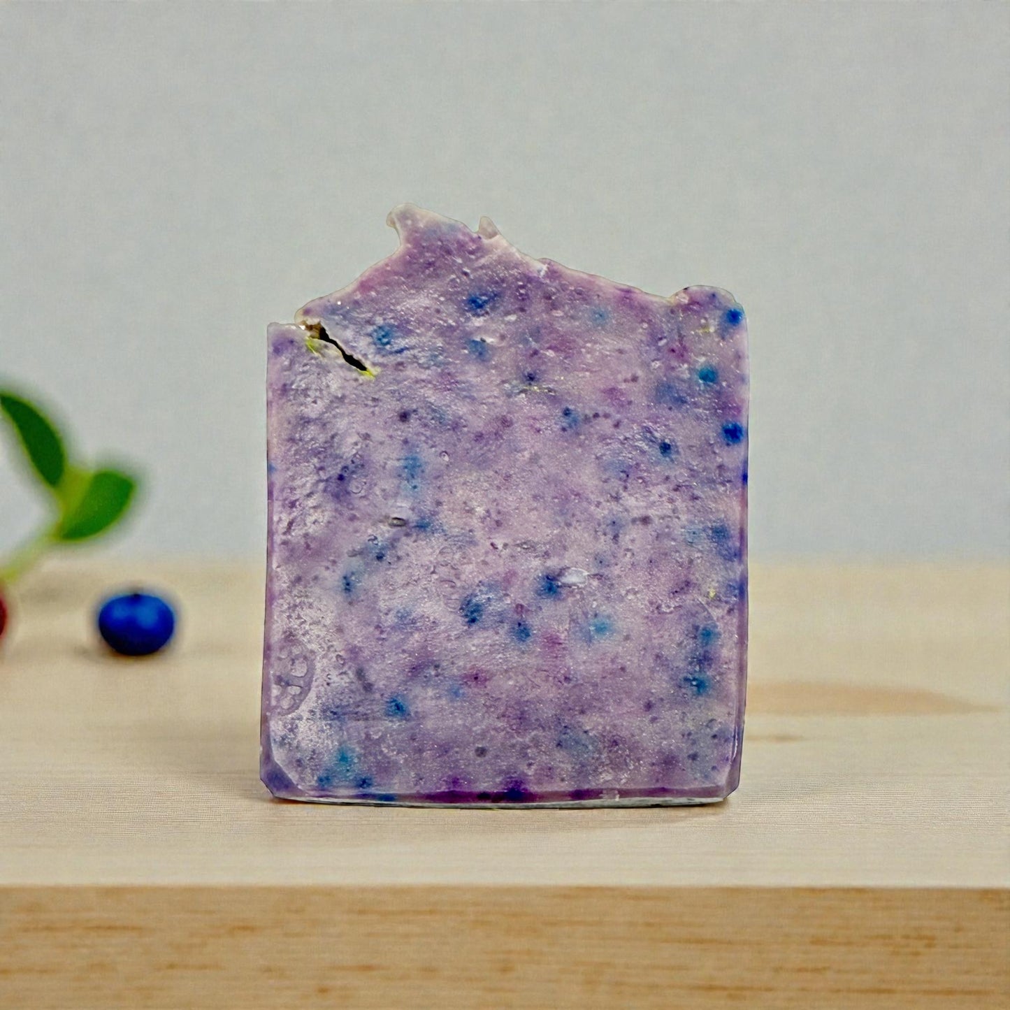 Purple speckled soap bar on a wooden surface with a light gray background