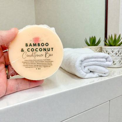 Hand holding a bamboo and coconut conditioner bar with a bathroom setting in the background.