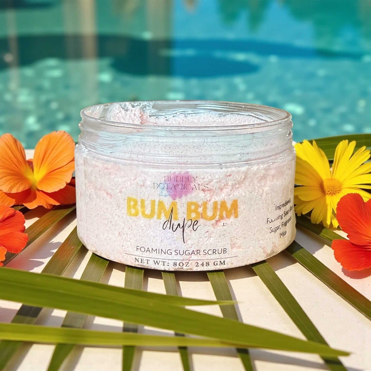 Jar of 'Bum Bum Dupe' foaming sugar scrub with flowers and pool in the background
