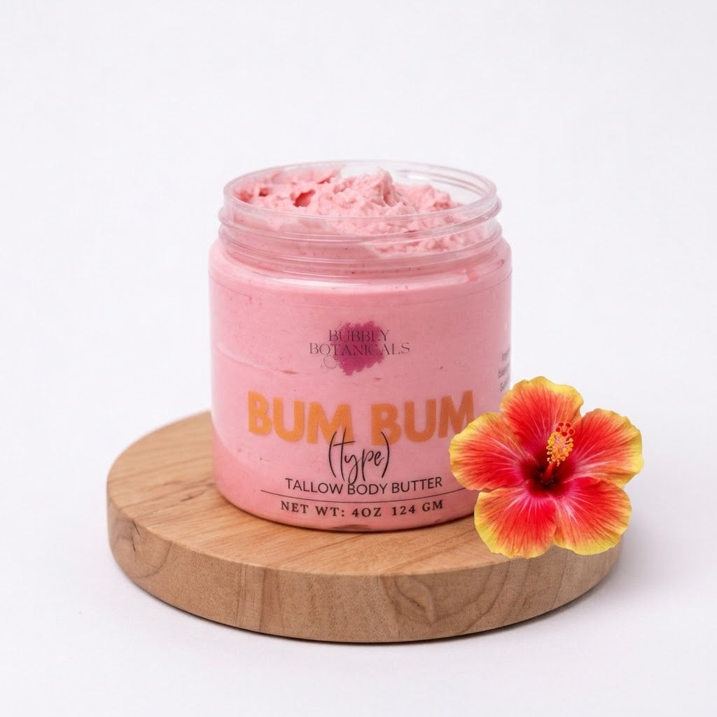 A jar of pink tallow body butter by Bubbly Botanicals, labeled 'BUM BUM (type) TALLOW BODY BUTTER', sitting on a round wooden coaster next to a red and yellow hibiscus flower on a white background.
