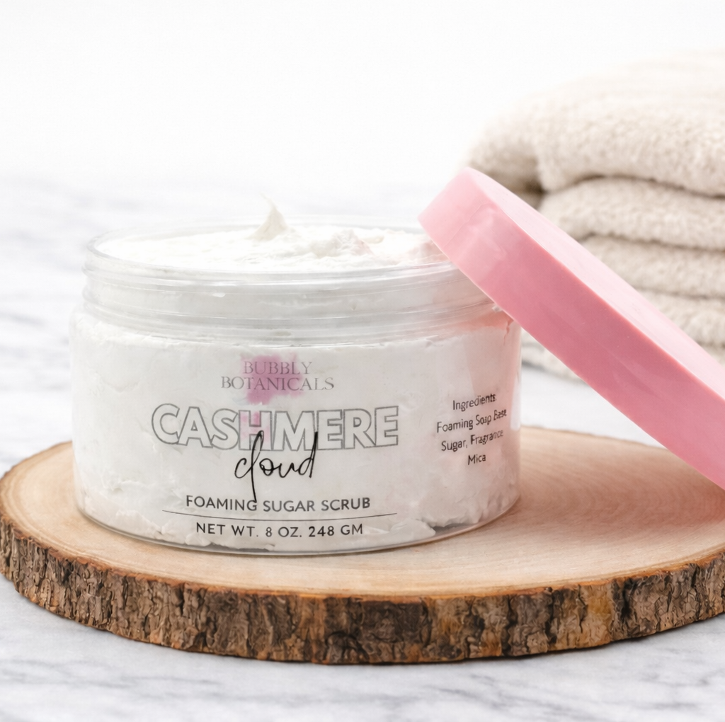 Jar of 'Cashmere Cloud' foaming sugar scrub with a pink scoop on a wooden block.