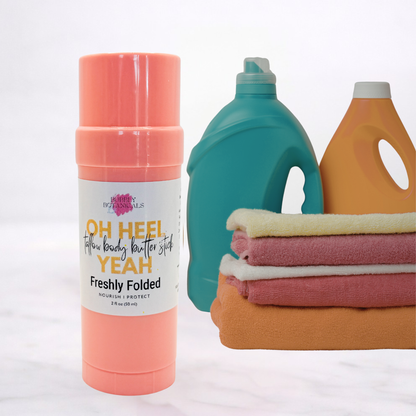 Coral body butter stick, teal bottle, and orange bottle with folded towels on a white background