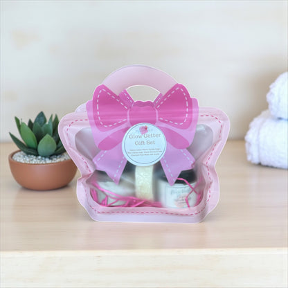 Pink gift set with a bow on a wooden surface, featuring a plant and white yarn ball in the background.