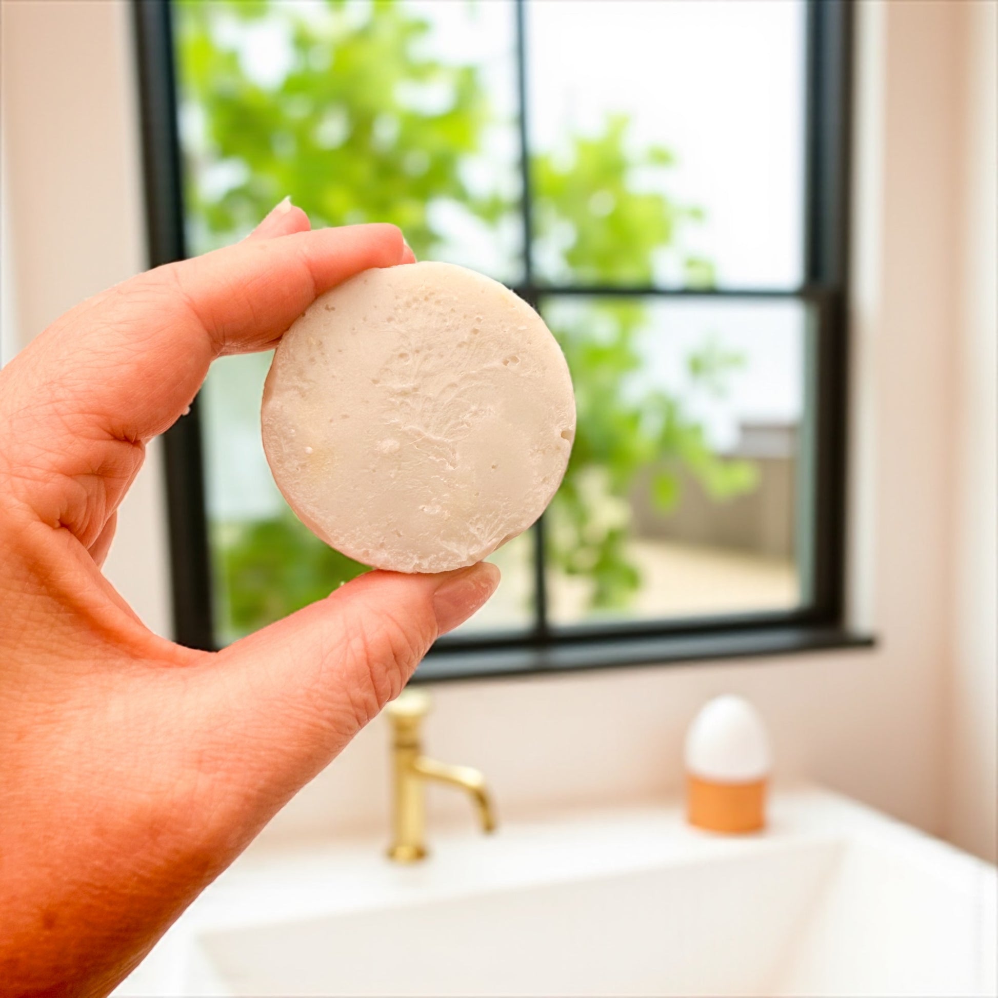 Mini tallow soap held up in a bathroom by a hand above