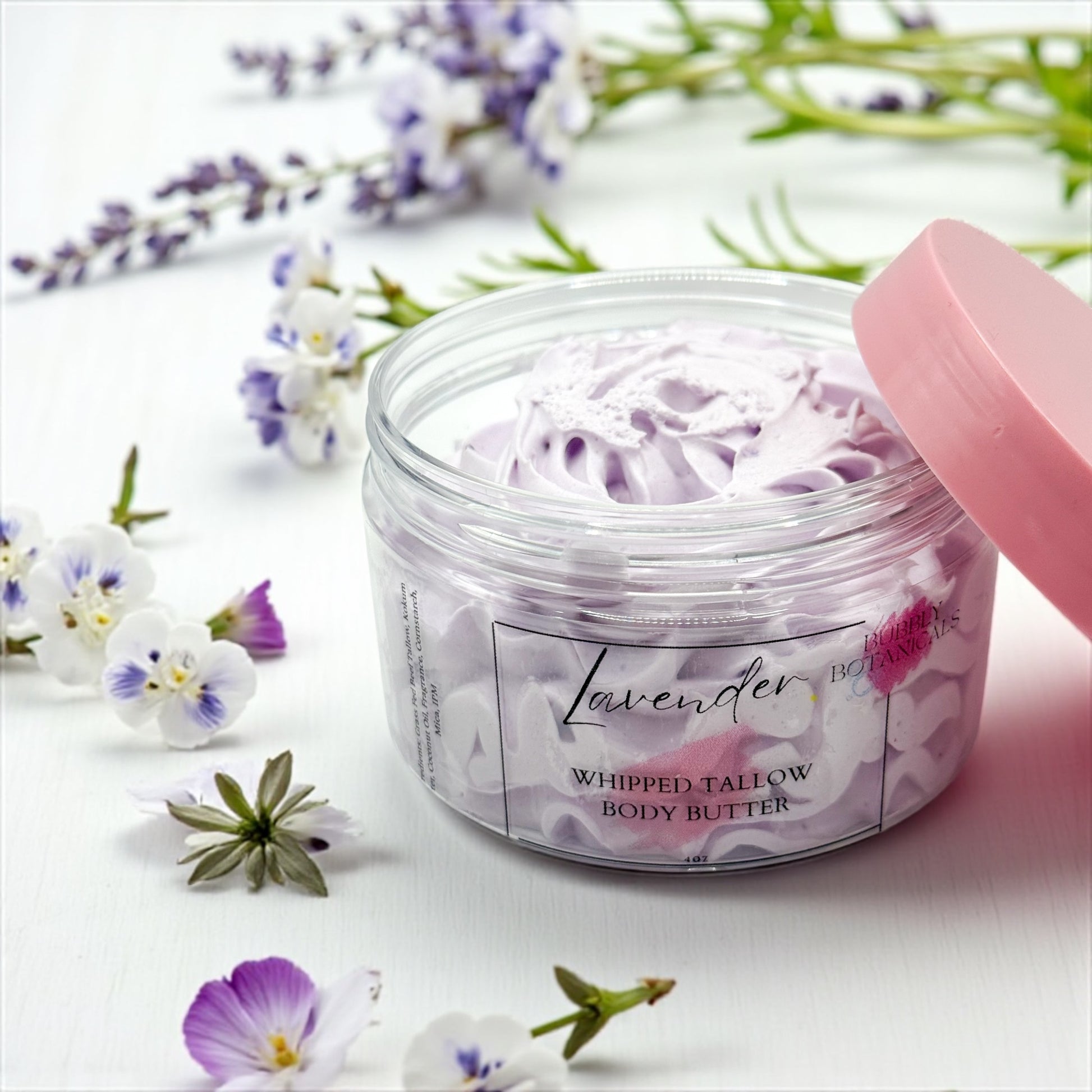 Jar of lavender whipped tallow body butter with a pink lid on a white background with flowers.