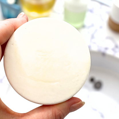 Hand holding a round white bar of soap with a blurred background