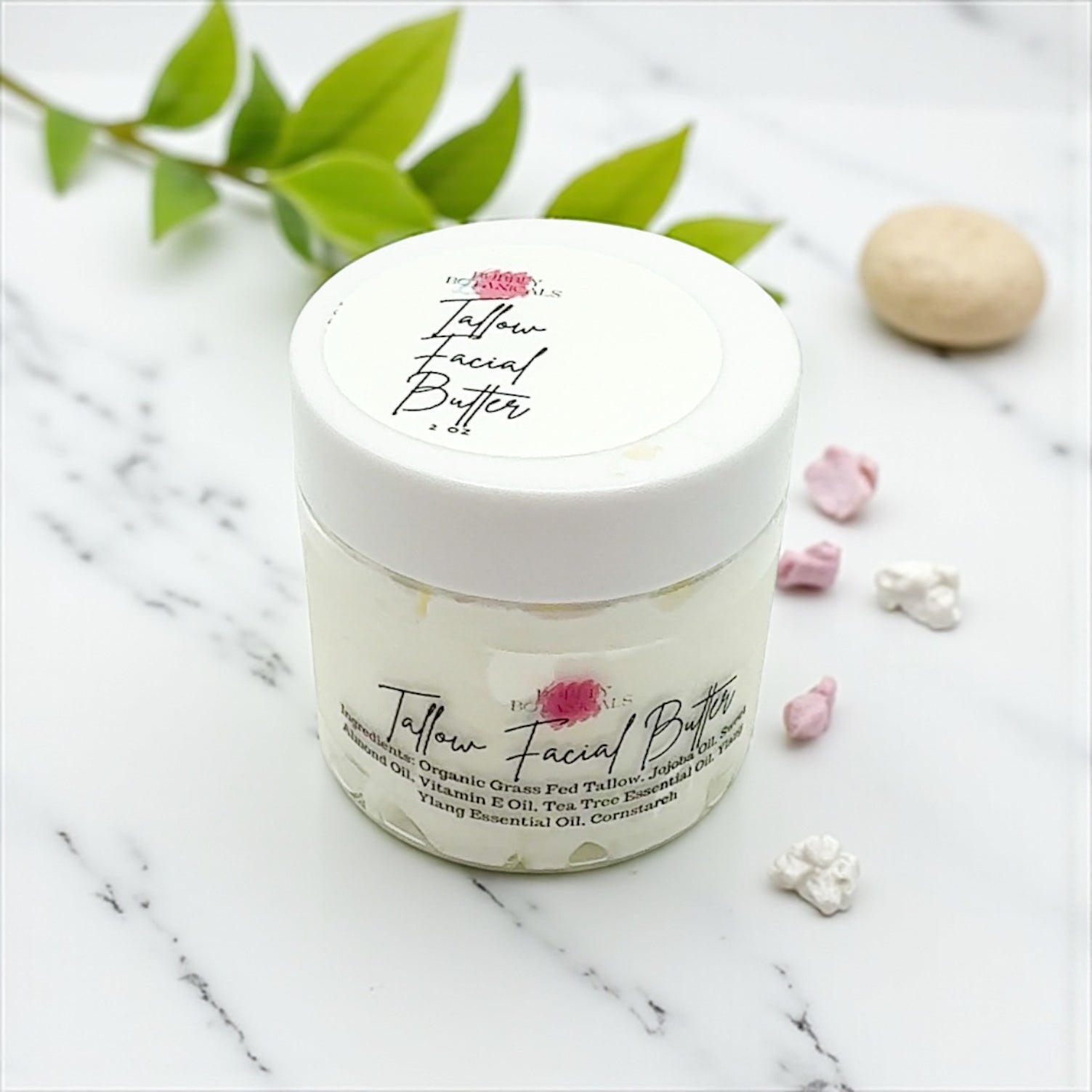 Jar of Jellow Facial Butter on a marble surface with green leaves and flowers.