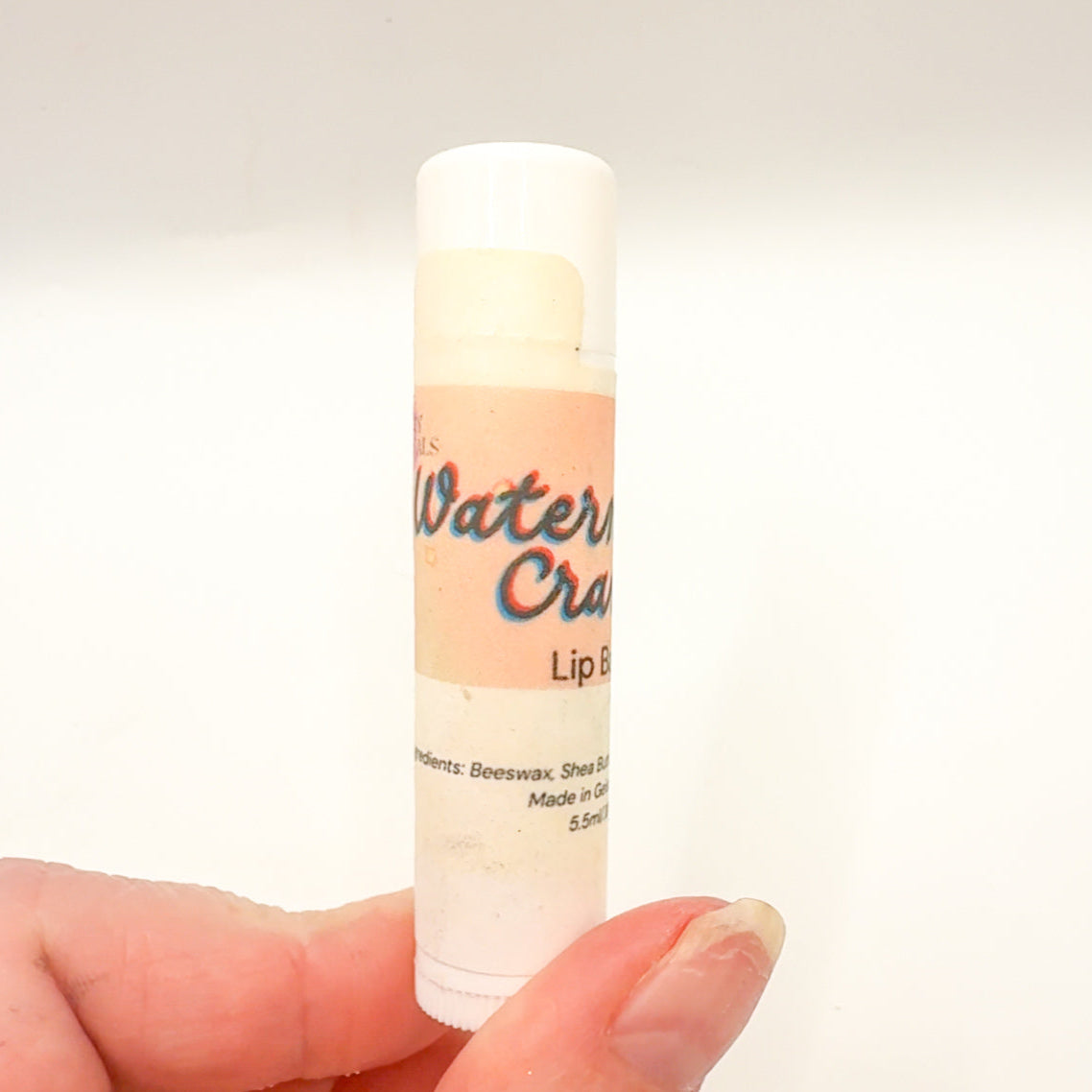 Lip balm stick held in a hand with a plain background