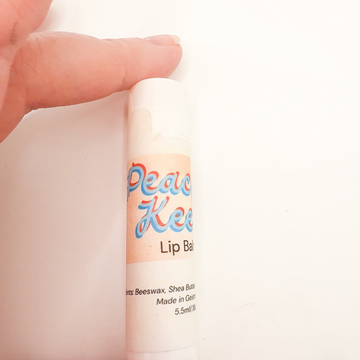 Lip balm with 'Peach Keen' branding held by a hand against a white background