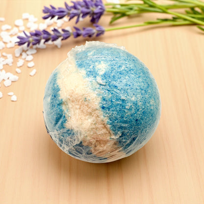 Blue and white bath bomb on a wooden surface with lavender flowers and white stones.