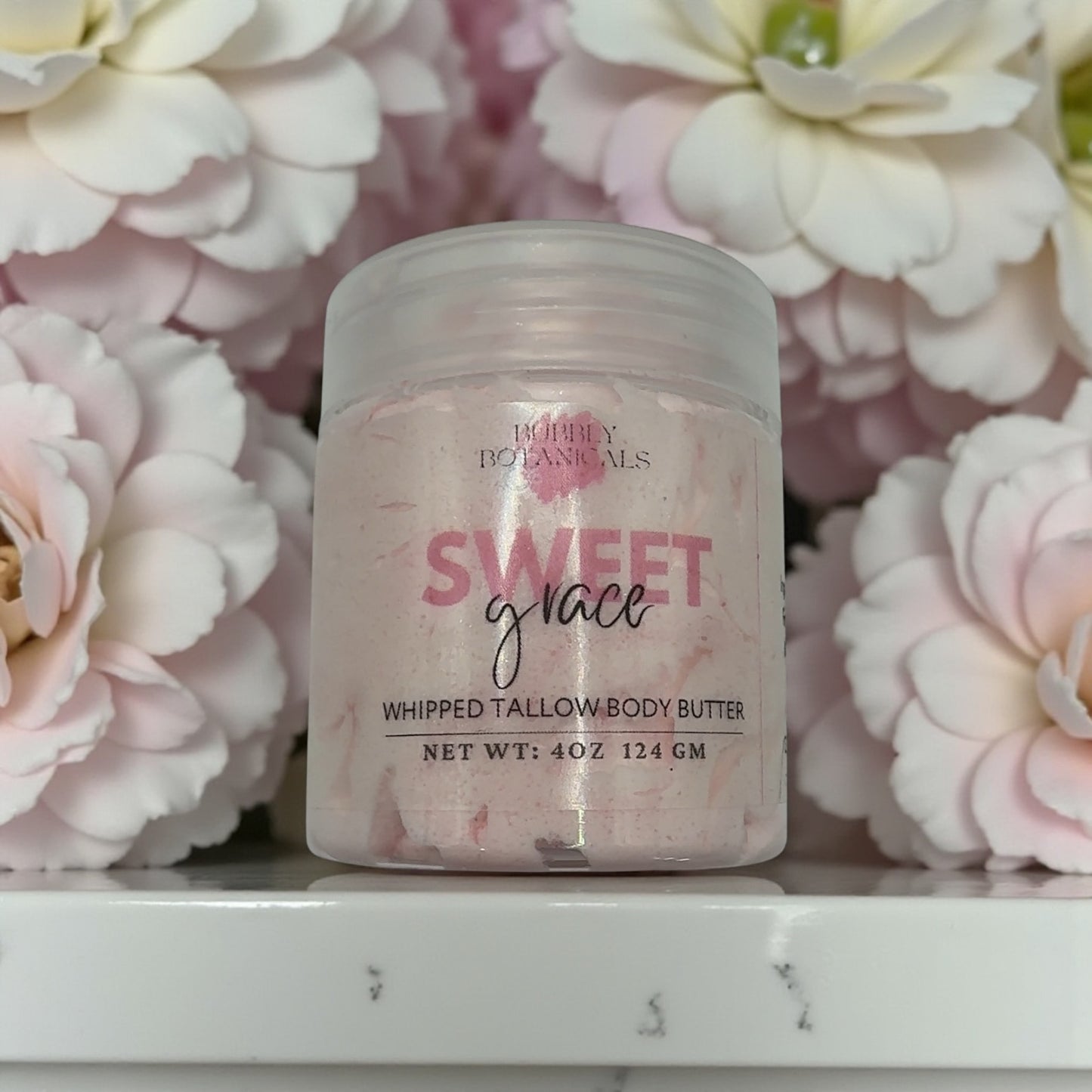 Jar of 'Sweet Grace' whipped tallow body butter with pink flowers in the background