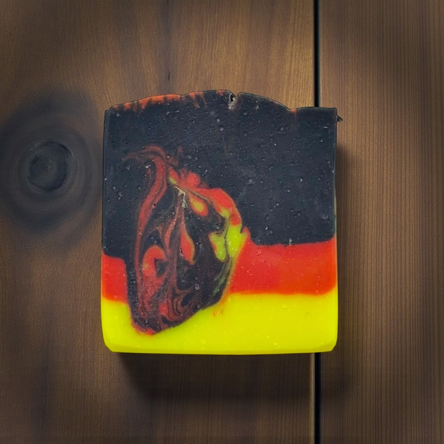 Soap bar with black, red, and yellow design on a wooden surface