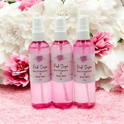 Three bottles of Pink Sugar hair fragrance and body mist with flowers in the background