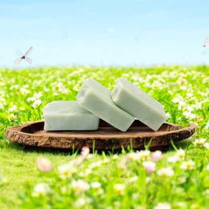 Three bars of soap on a wooden tray with a grassy field and flowers in the background
