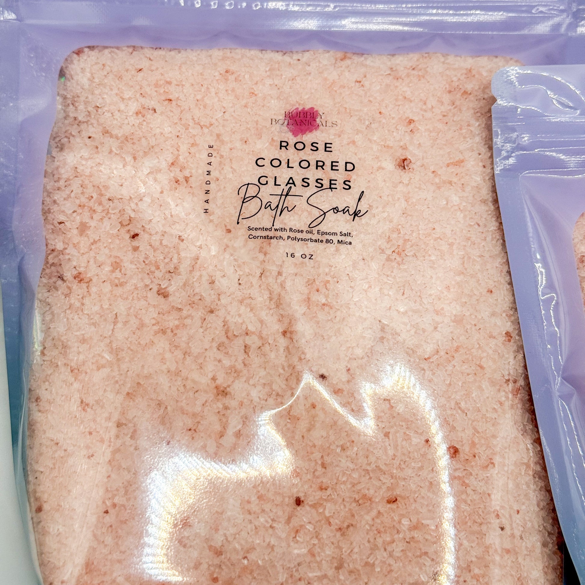 Rose-colored bath soak package with visible branding on a white background