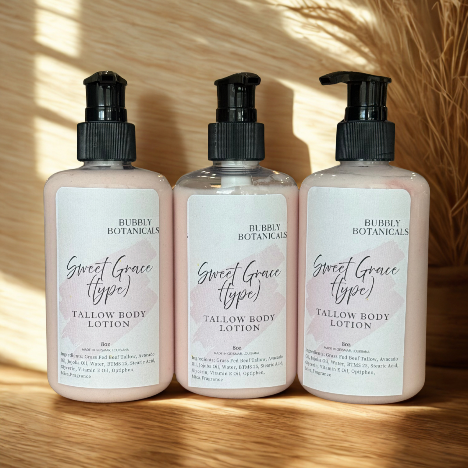 Three bottles of Bubly Botanicals Sweet Grace Tallow Body Lotion on a wooden surface with sunlight casting shadows.