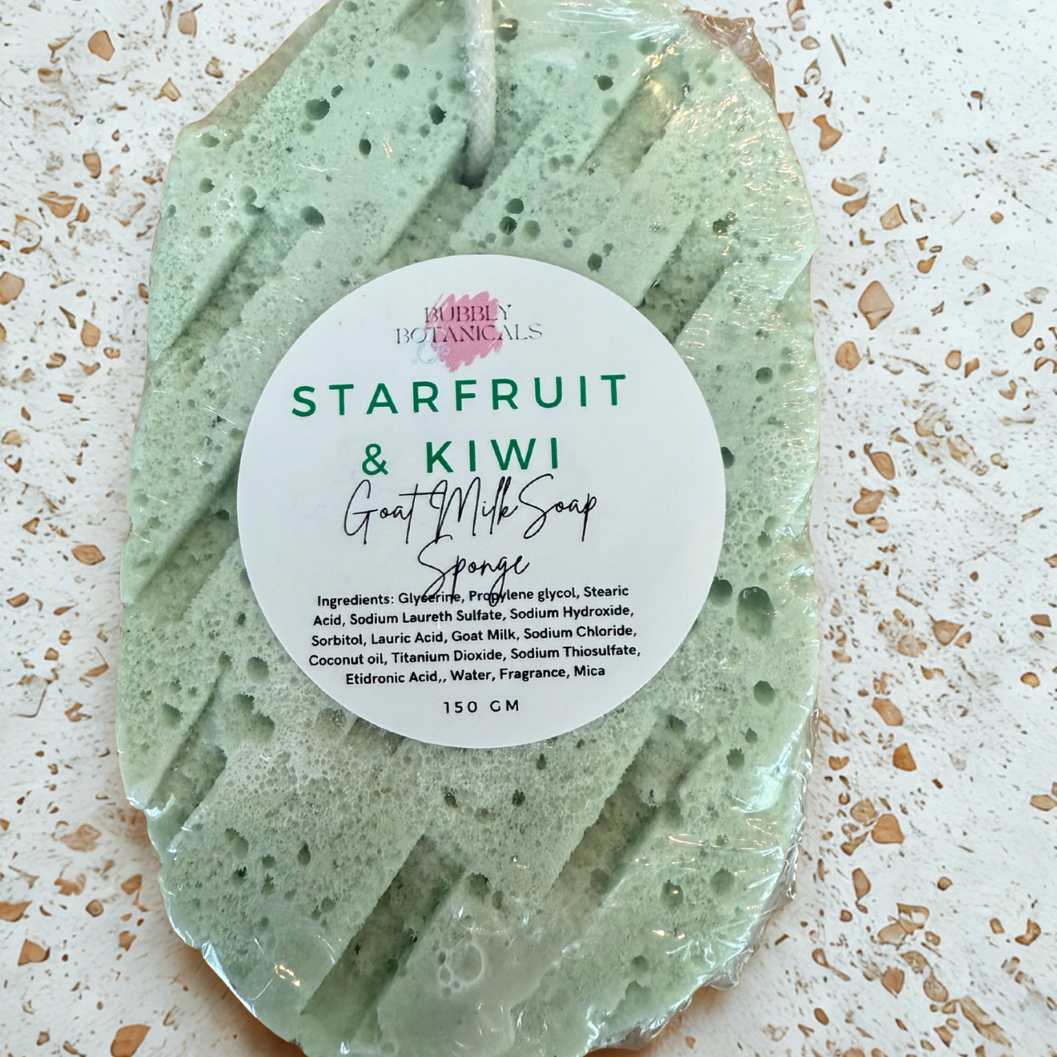 Green starfruit and kiwi soap sponge with a label on a textured beige surface