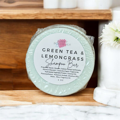 Green tea and lemongrass shampoo bar with a label on a wooden shelf.