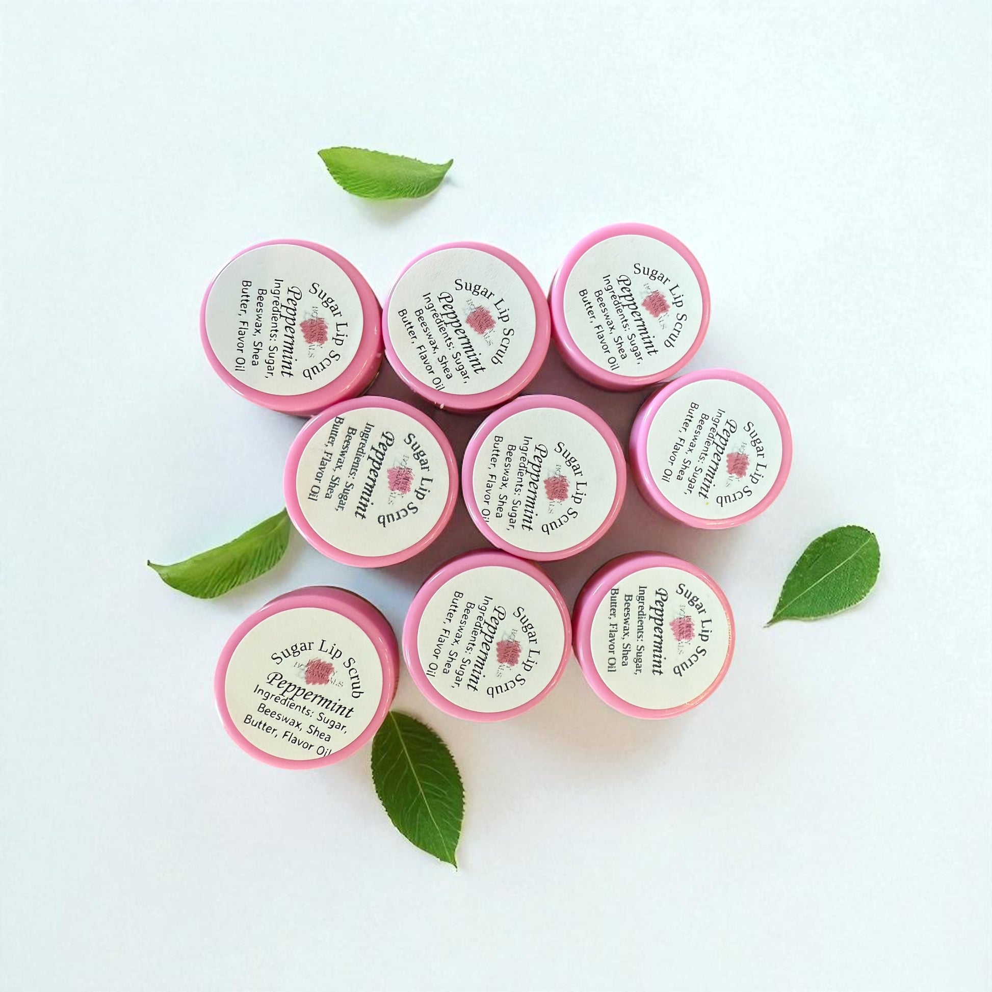 Pink lip balm containers with green leaves on a light background