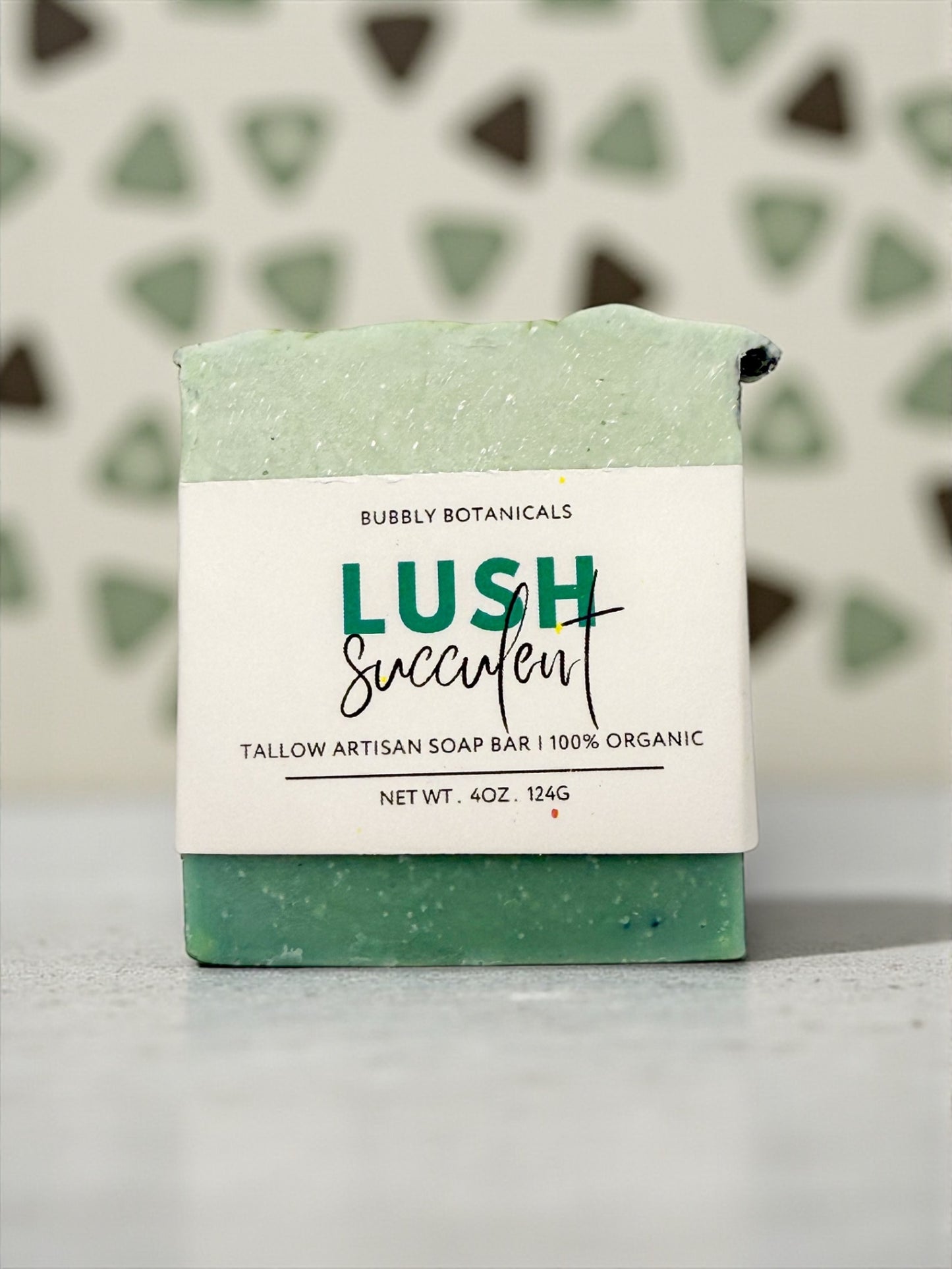 Green soap bar with a white label on a gray surface, against a patterned wall.