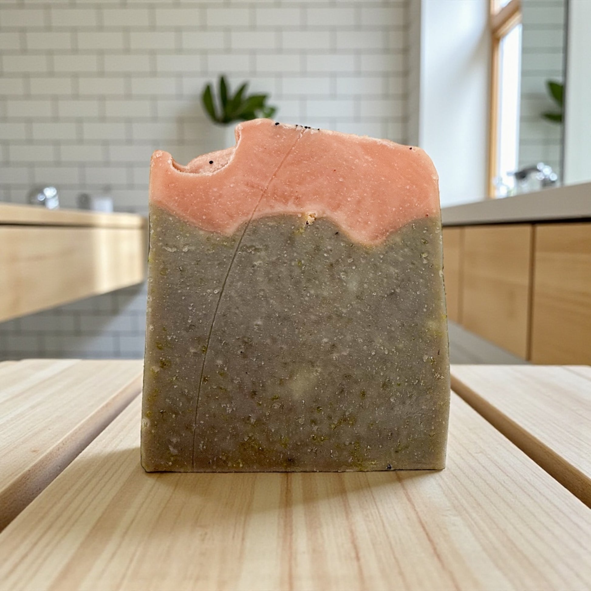 Bar of soap with a pink top and brownish bottom on a wooden surface, kitchen in the background