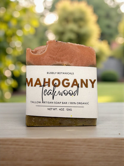 Bar of soap labeled 'Mahogany Teakwood' by Bubly Botanicals on a wooden surface with a blurred natural background.
