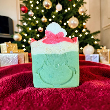 A mister grinch tallow soap with a grinch face in front of a Christmas tree