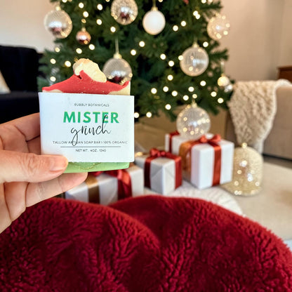 Hand holding a mister grinch tallow soap in front of a Christmas tree