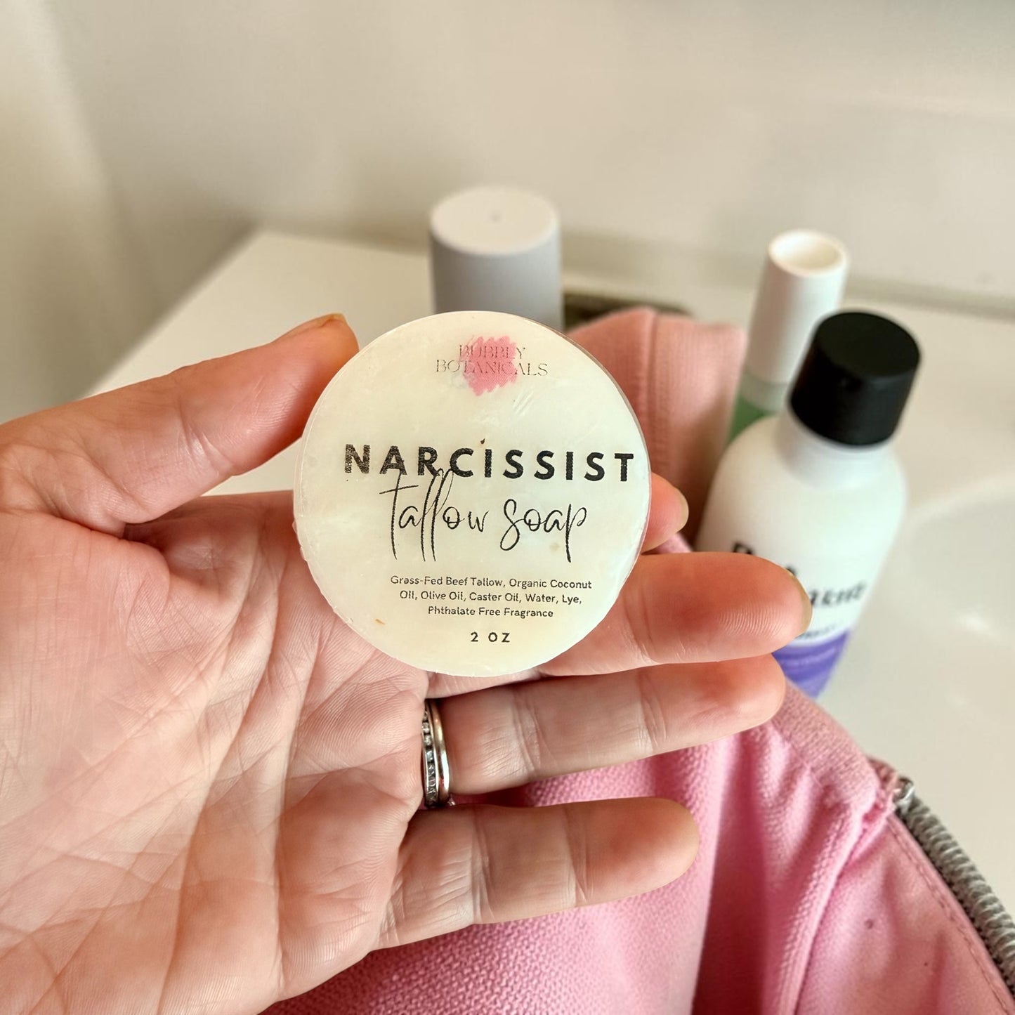 Hand holding narcissist scented travel tallow soap by bubbly botanicals, packing it into a toilet bag