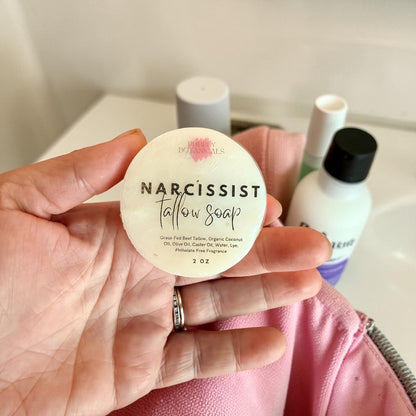 Hand holding narcissist scented travel tallow soap by bubbly botanicals, packing it into a toilet bag