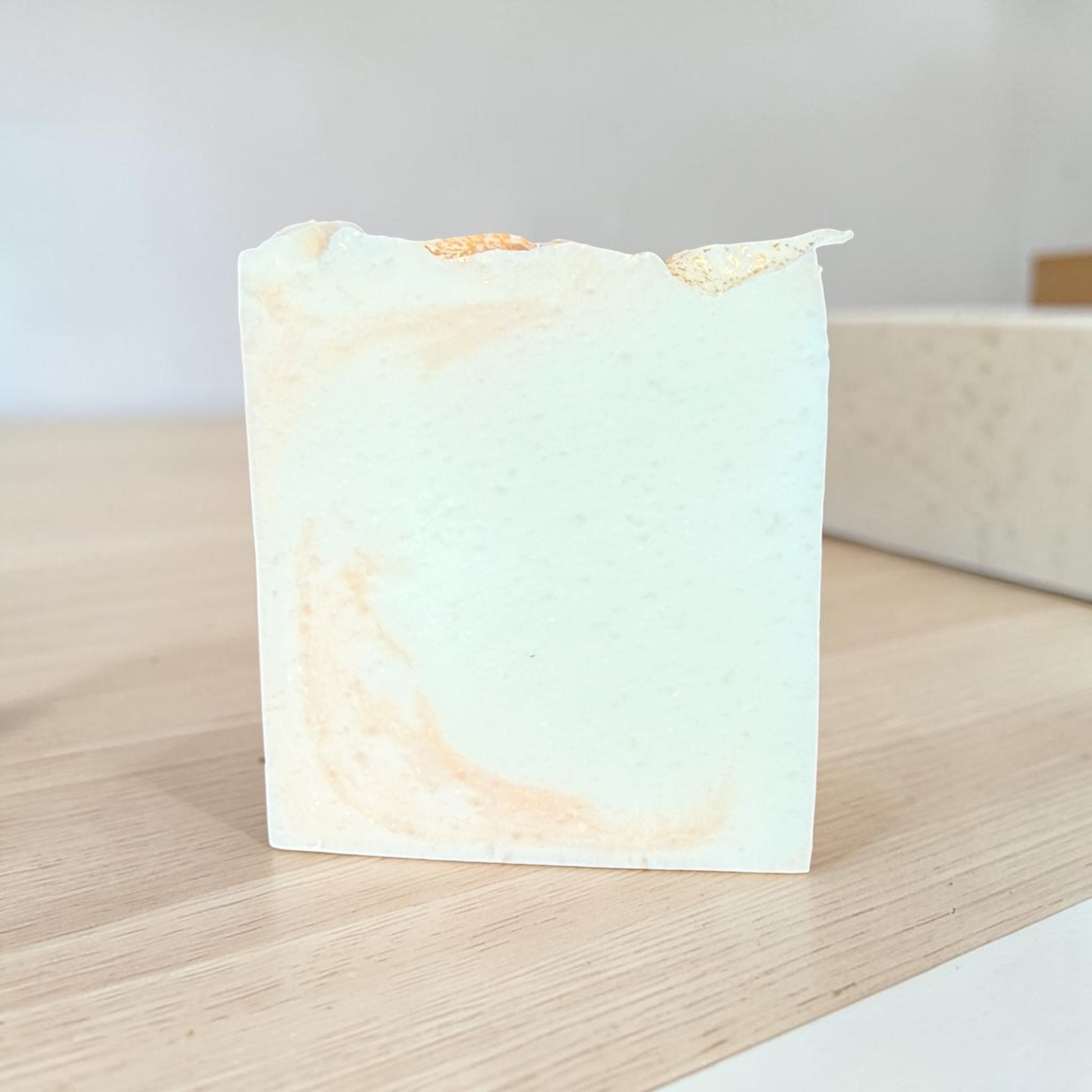 A rectangular bar of handmade tallow soap in the Narcissist type scent with a pale base and light peach swirls, standing on a light wood surface.