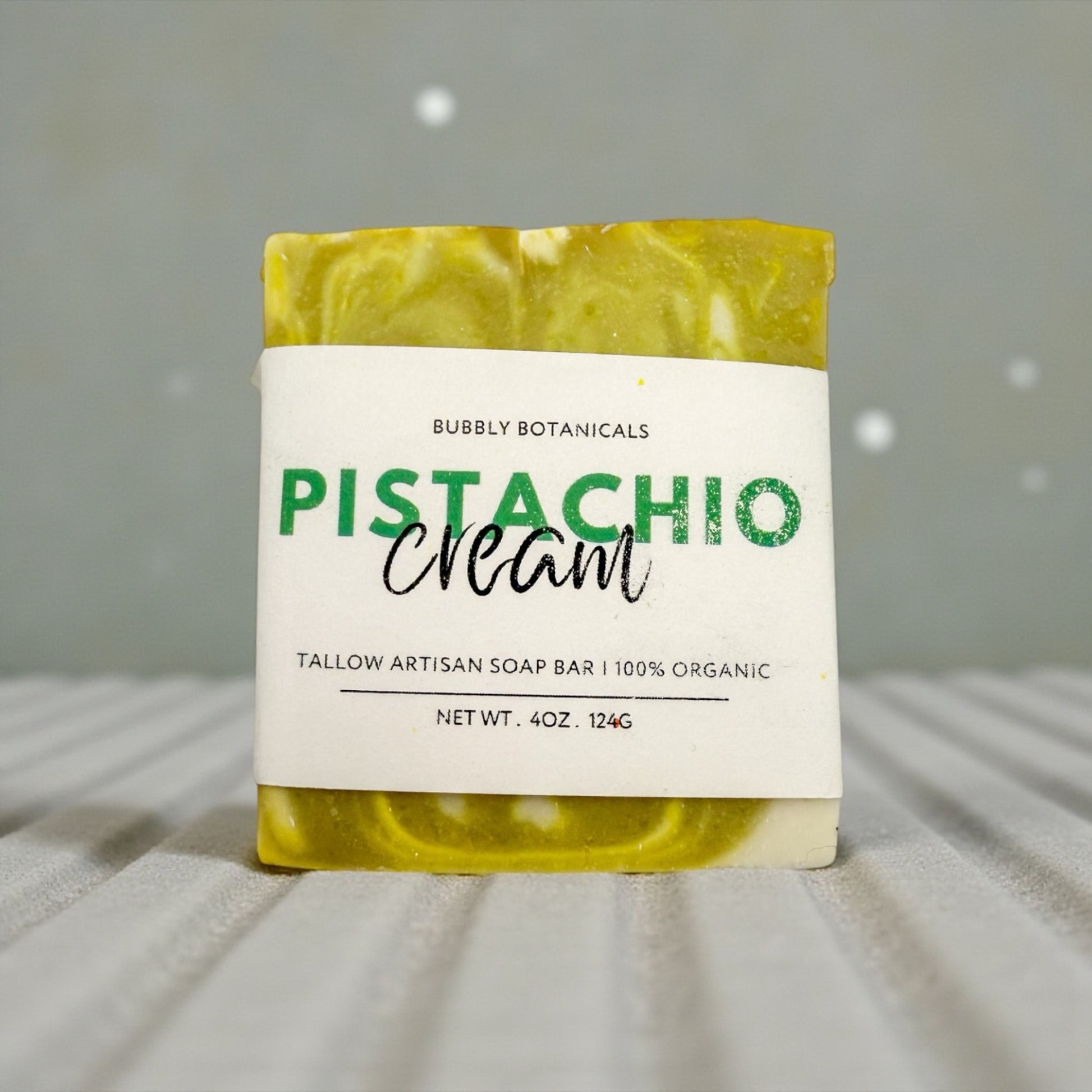 Bar of soap with a label indicating 'Pistachio Cream' from Bubbly Botanicals on a neutral background.
