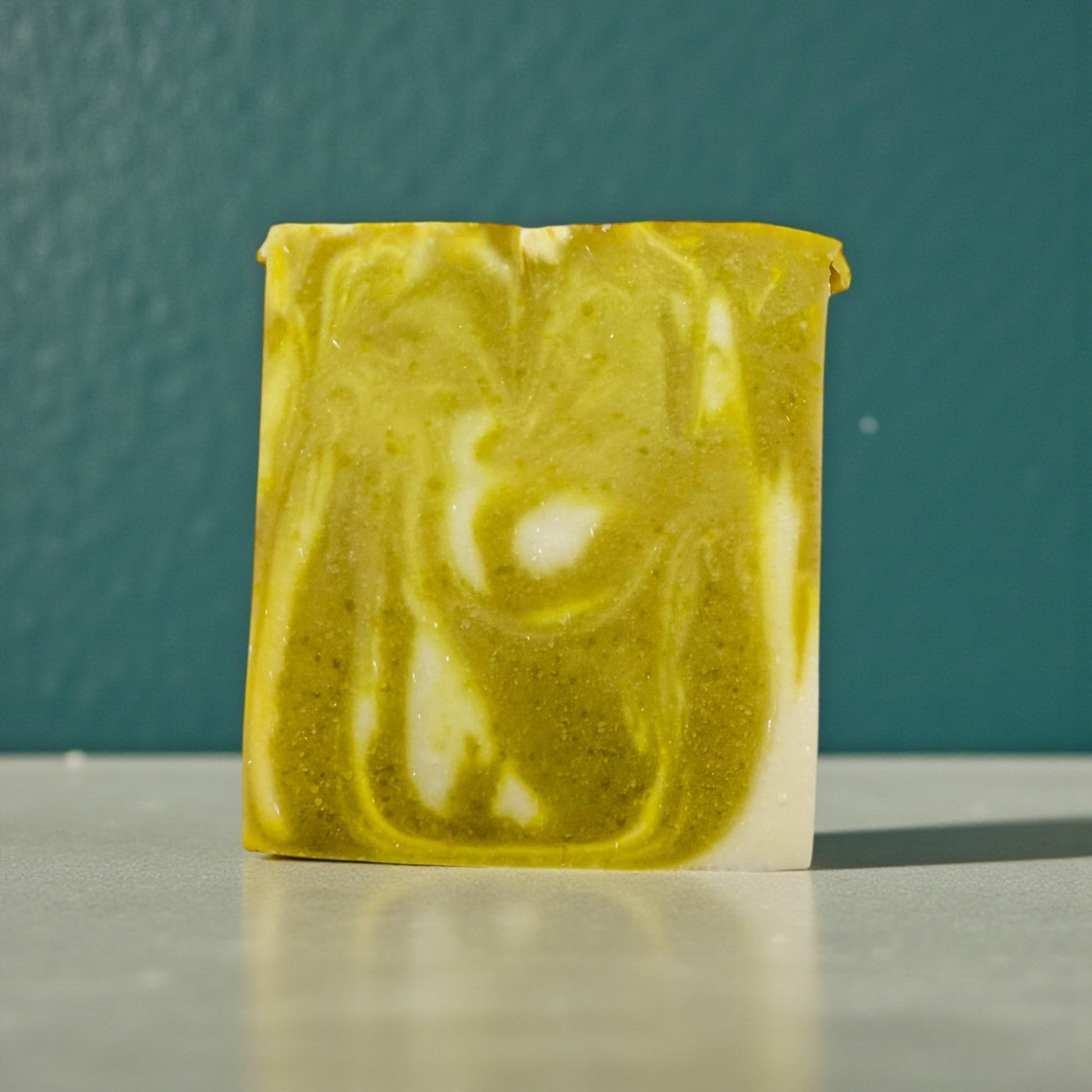 Marbled green and white soap bar on a reflective surface with a teal background