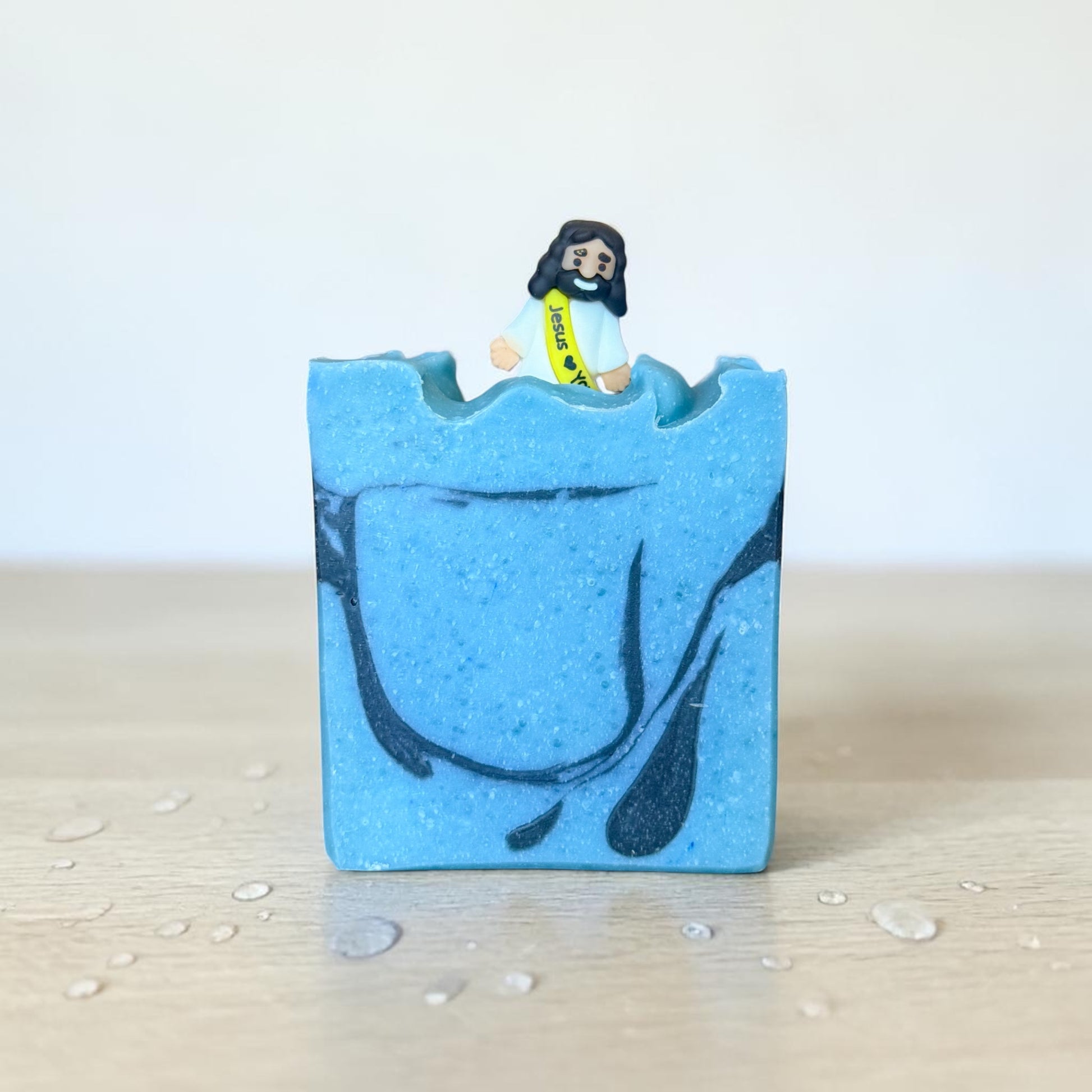 Sacred Sea tallow soap bar with blue and black swirl design and Jesus figure walking on water topper, ocean scented handmade soap