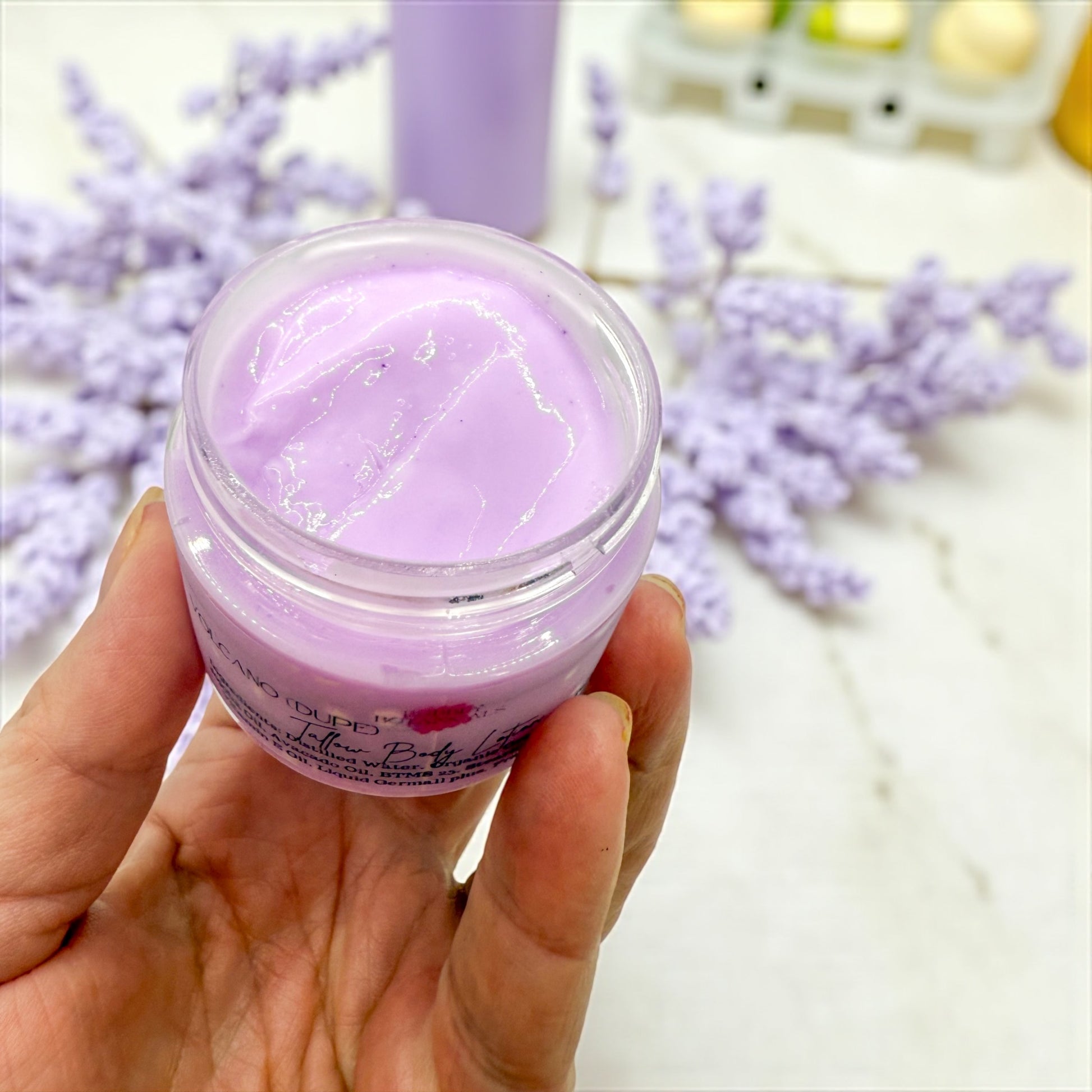 Hand holding a jar of purple cream with lavender flowers in the background
