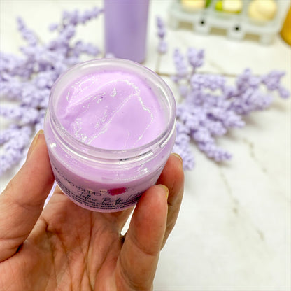 Hand holding a jar of purple cream with lavender flowers in the background