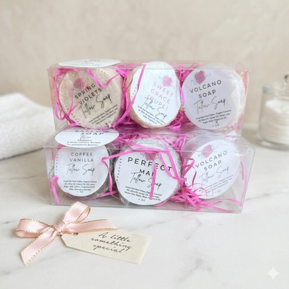 Set of wrapped soaps with labels in a clear box on a marble surface.