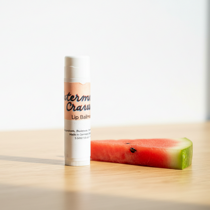 Lip balm with watermelon flavor on a wooden surface next to a slice of watermelon.