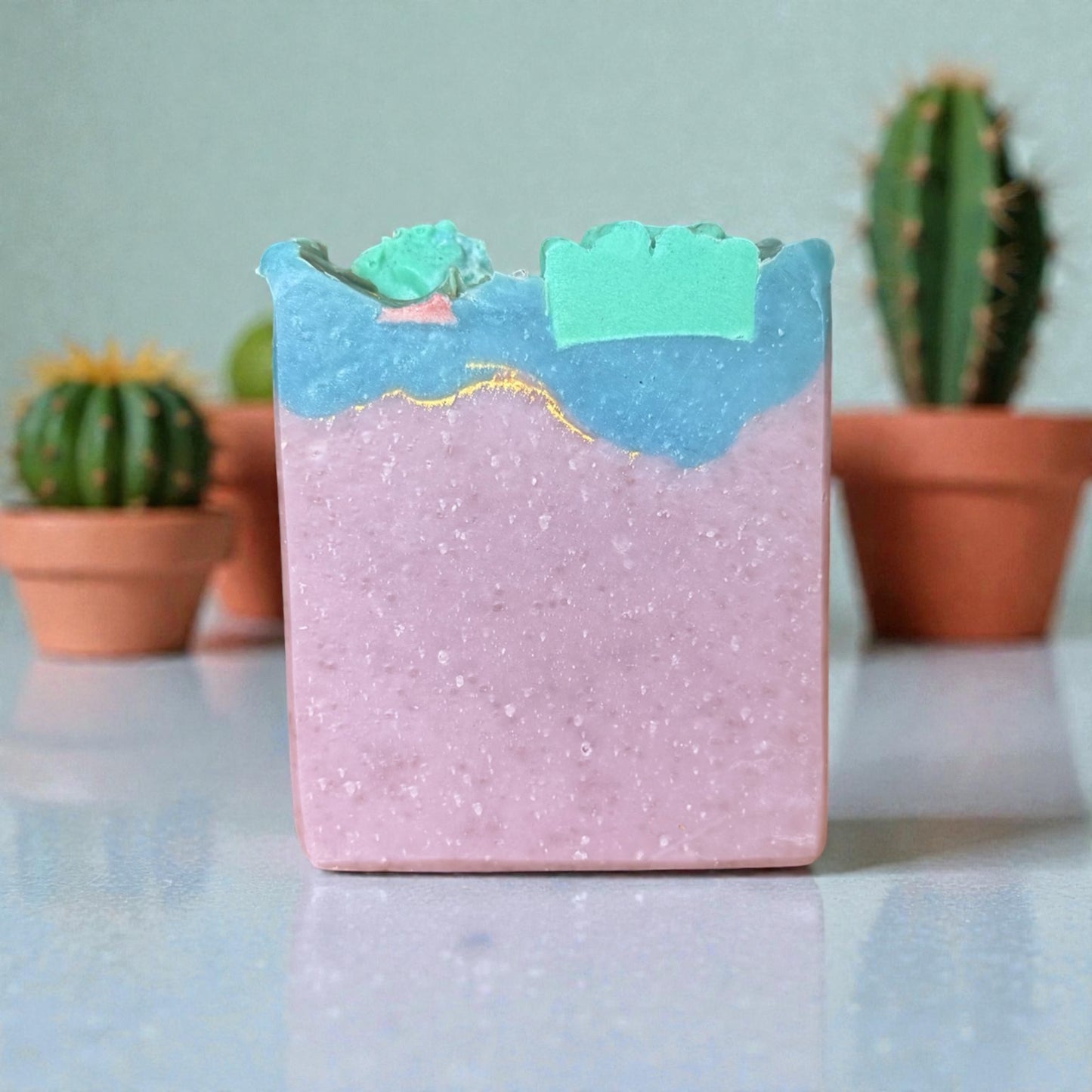 Bar of cactus blossom tallow soap with a mountain design on a reflective surface with cacti in the background