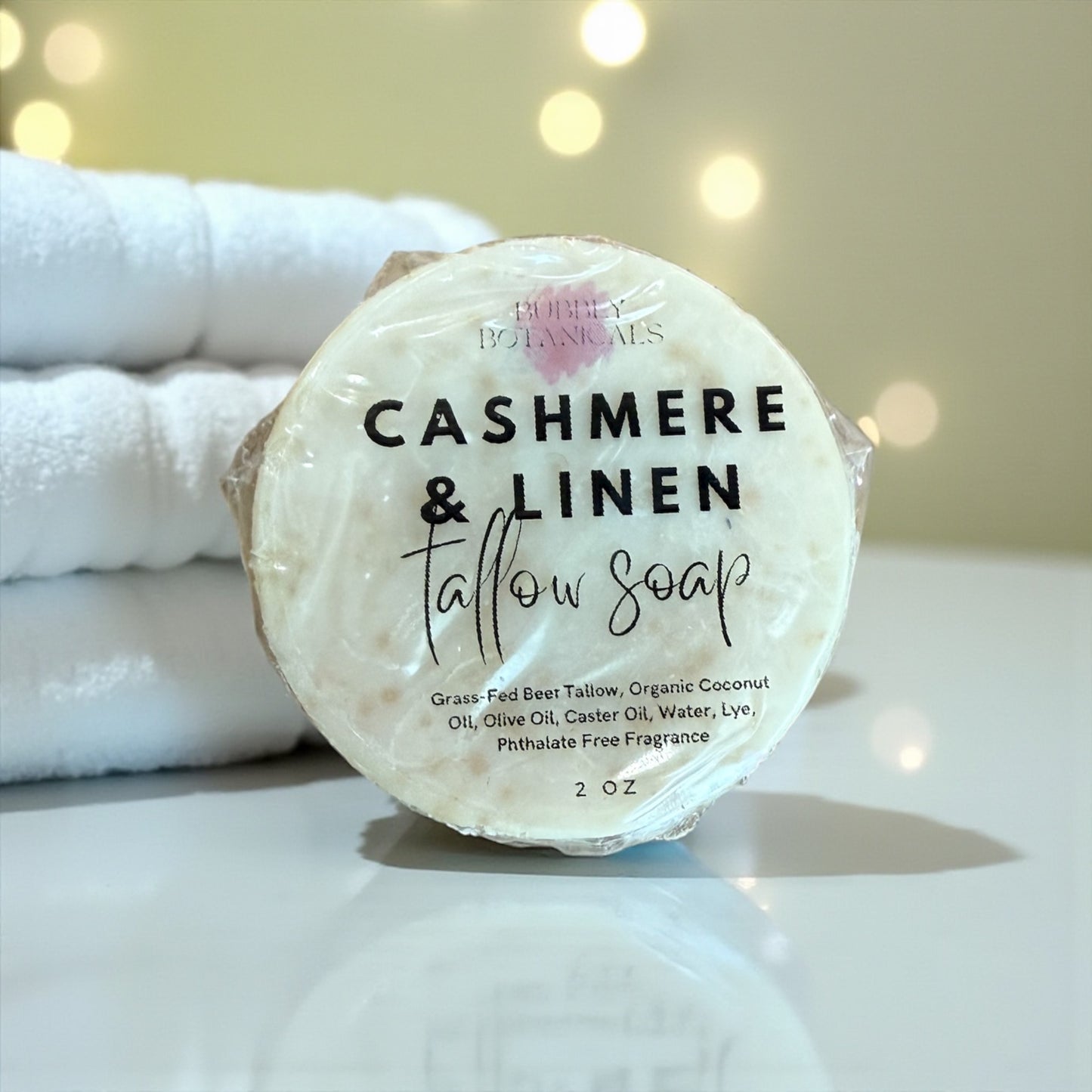Tallow soap bar labeled 'Cashmere & Linen' with a stack of white towels in the background.